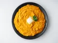 Un cremoso puré de boniato, coronado con una pastilla de mantequilla y una ramita de perejil, listo para disfrutar.