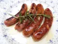 Salchichas al vino Monsieur Cuisine, doradas y jugosas, con romero fresco sobre un plato blanco con motivos azules.