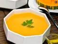 Un cremoso y vibrante **pure de calabaza** en un cuenco blanco, decorado con perejil fresco. Al fondo, un trozo de calabaza y una cuchara.