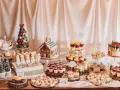 Mesa llena de postres navideños: casa de jengibre, árbol de macarons, muñecos de nieve, cupcakes y galletas.
