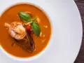 Un plato de zarzuela de pescado con gambas, mejillones y tomate, decorado con albahaca fresca.