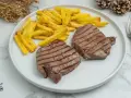 Dos jugosos solomillos de ternera a la plancha, con marcas de parrilla, acompañados de patatas fritas doradas.