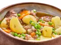 Un reconfortante ragú con trozos de carne tierna, patatas, zanahorias y guisantes en un cuenco rústico.