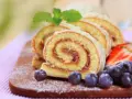 Brazo de gitano en rodajas con fresas y arándanos sobre tabla de madera.