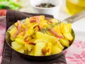 Patatas al microondas con trocitos de bacon crujiente y romero fresco, servidas en una sartén metálica. ¡Un plato sencillo y delicioso!