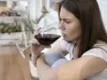 Mujer pensativa bebe vino tinto, recordando que el vino engorda.