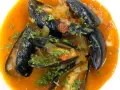 Mejillones a la marinera, jugosos y frescos, nadan en una salsa roja vibrante con perejil picado.
