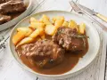 Dos tiernas porciones de pata de ternera guisada en su jugo, acompañadas de patatas rústicas fritas y una ramita de tomillo.