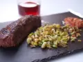 Un jugoso onglet de ternera a la parrilla, acompañado de verduras salteadas y una guarnición rojiza.