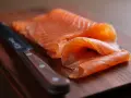 Finísimas lonchas de salmón marinado, listas para disfrutar, junto a un cuchillo de chef sobre tabla de madera.