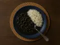 Plato de calamares en su tinta con arroz blanco, servido en un plato azul sobre una esterilla de mimbre.