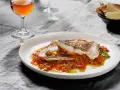 Deliciosa urta a la roteña servida en plato blanco, con vino y pan tostado al fondo.