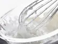 Batidor de varillas mezclando **nata montada** en un bol de cristal.
