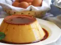 Delicioso flan de huevo casero con caramelo líquido, decorado con menta. En el fondo, una cesta con huevos frescos.
