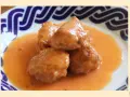 Deliciosas albóndigas de rape en una cremosa salsa naranja, servidas en un plato con borde azul.