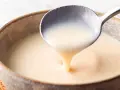 Cuchara sirviendo crema inglesa cremosa en un cuenco rústico.