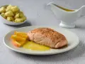 Filete de salmón a la naranja, servido con gajos de naranja y una salsa dorada. Acompañado de gnocchis en un cuenco.