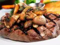 Solomillo de ternera guisado con champiñones salteados y perejil picado, servido en un plato blanco.