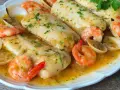Merluza a la marinera con gambas y almejas, todo bañado en una deliciosa salsa dorada y espolvoreado con perejil fresco.