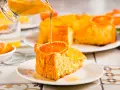 Un trozo de tarta de naranja esponjosa, decorado con una rodaja de naranja y bañado en un almíbar dorado.