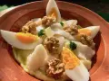 Delicioso plato de atascaburras receta con huevo duro, nueces y perejil en una cazuela de barro.