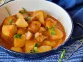 Un reconfortante plato de patatas con bacalao en una salsa rojiza, adornado con perejil fresco.