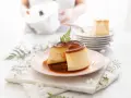Delicioso flan de queso con caramelo líquido, decorado con una ramita verde. Se apilan más porciones en el fondo.