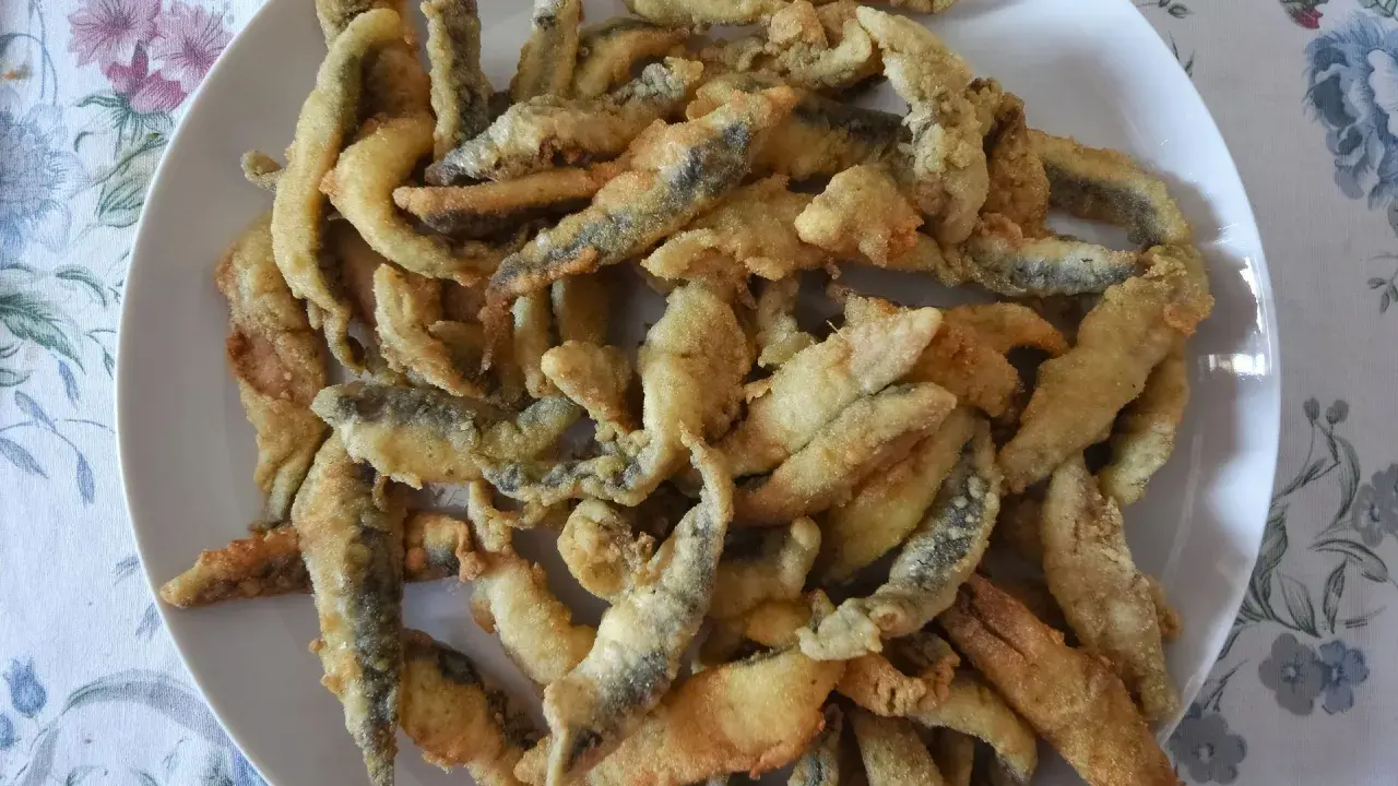 Un plato blanco lleno de boquerones fritos crujientes, listos para disfrutar.