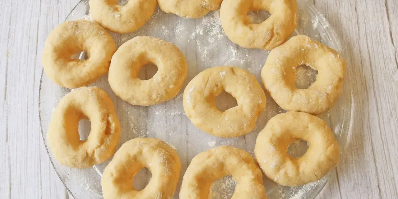 Un plato transparente muestra rosquillas caseras esponjosas, listas para hornear.