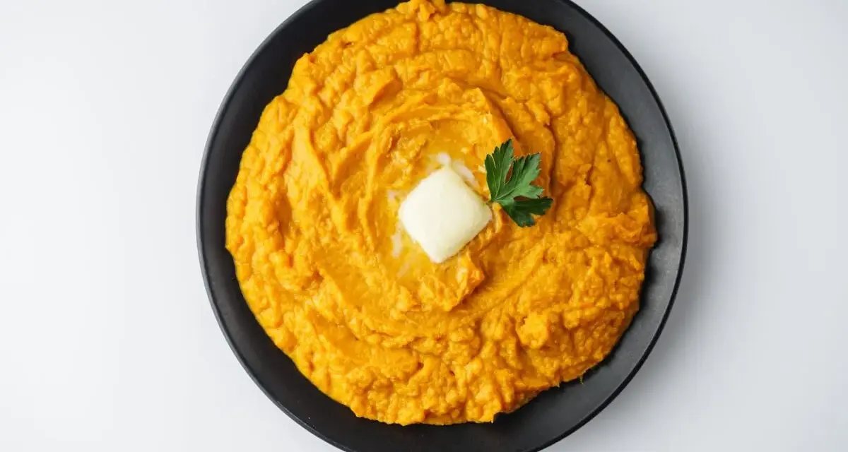 Un cremoso puré de boniato, coronado con una pastilla de mantequilla y una ramita de perejil, listo para disfrutar.