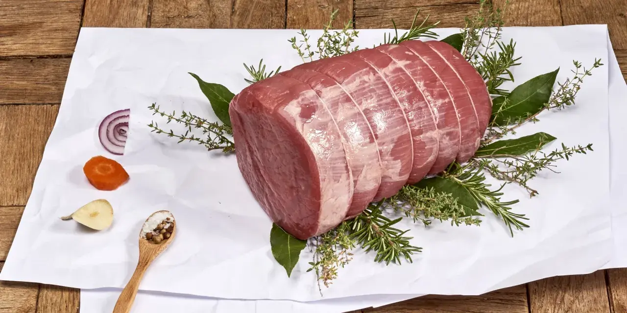 Un añojo ternera, parte de la pierna, listo para asar con hierbas aromáticas, cebolla, zanahoria y especias.