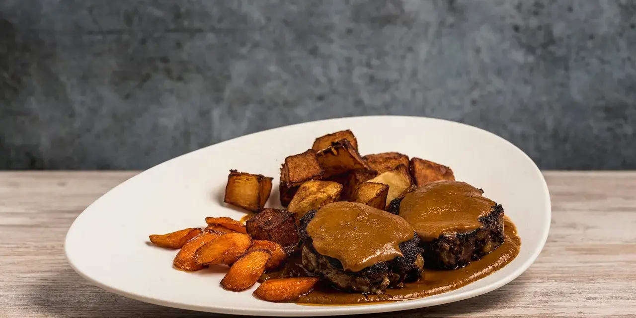 Delicioso plato de cola de toro en salsa, acompañado de patatas rústicas y zanahorias glaseadas.