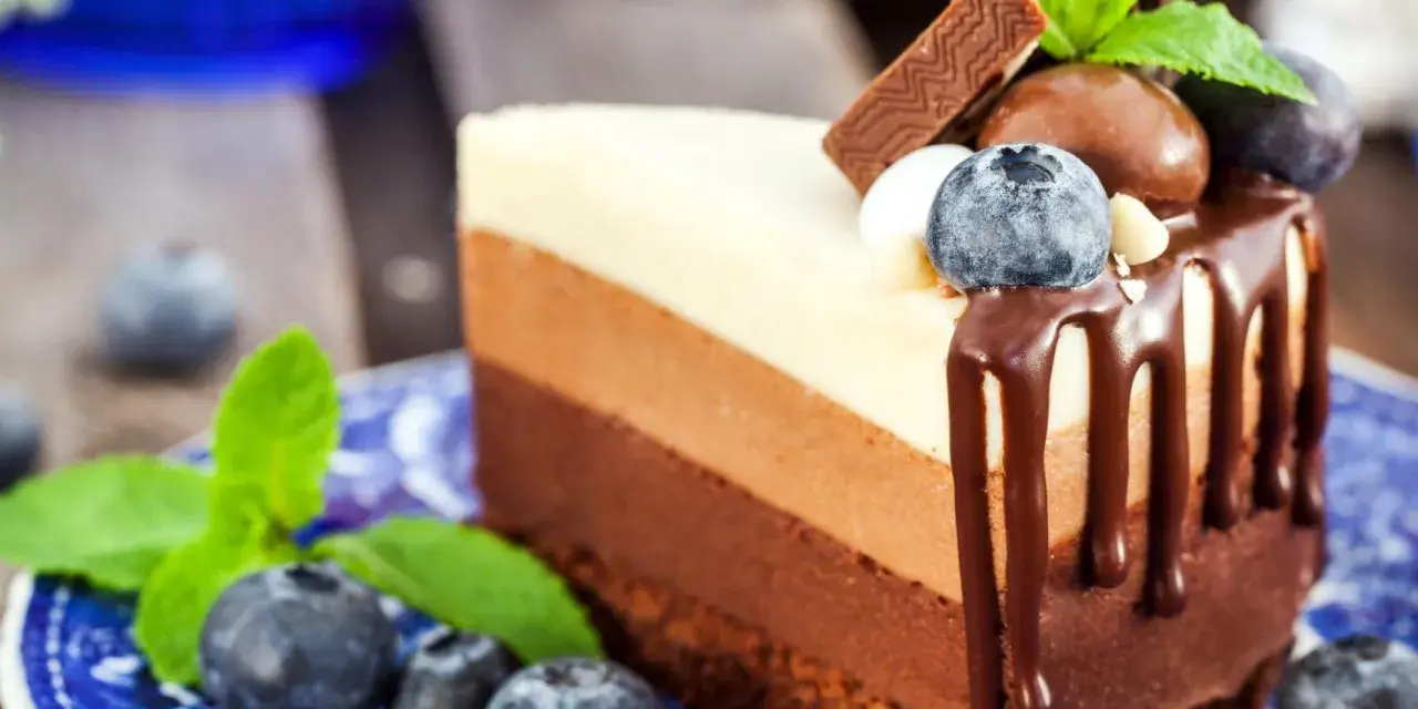 Deliciosa tarta de tres chocolates, con capas de chocolate blanco, con leche y negro, decorada con arándanos y menta.