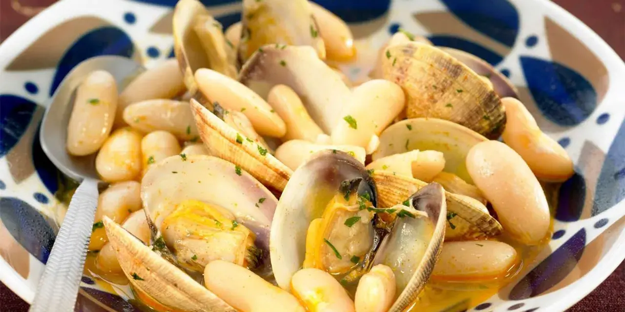 Un plato humeante de fabes con almejas, con judías blancas tiernas y almejas jugosas en una salsa dorada, adornado con perejil picado.