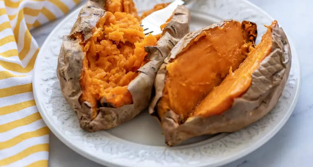 Dos mitades de boniato asado en freidora de aire, servidas en un plato blanco con un tenedor.