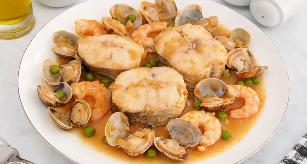 Merluza a la cazuela con gambas, almejas y guisantes en una salsa sabrosa.