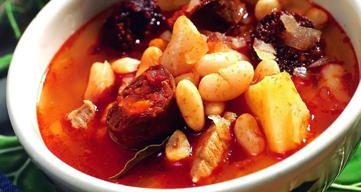 Un reconfortante plato de alubias con chorizo, trozos de morcilla y patatas en un cuenco blanco.