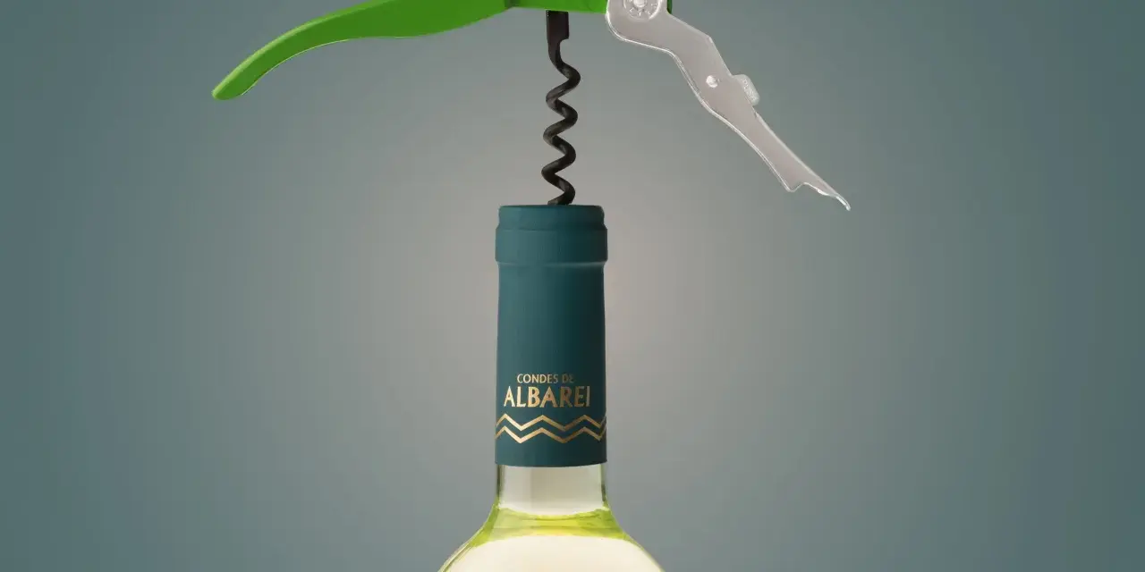 Sacacorchos verde y plateado sobre una botella de vino blanco "Condes de Albarei". El sacacorchos está listo para extraer el corcho, recordándonos de donde viene el corcho.