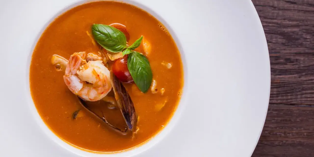 Un plato de zarzuela de pescado con gambas, mejillones y tomate, decorado con albahaca fresca.
