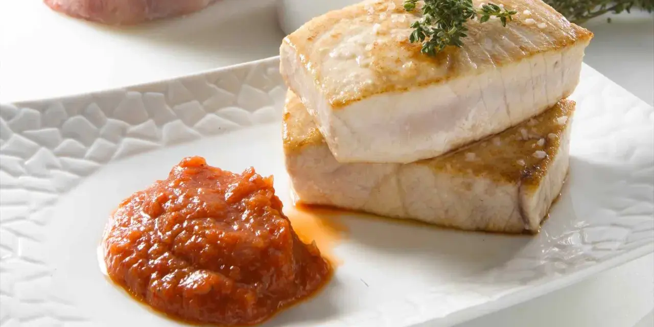 Dos trozos de atún a la plancha apilados, con una cucharada de salsa de tomate y una ramita de tomillo.