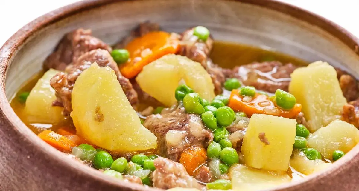 Un reconfortante ragú con trozos de carne tierna, patatas, zanahorias y guisantes en un cuenco rústico.