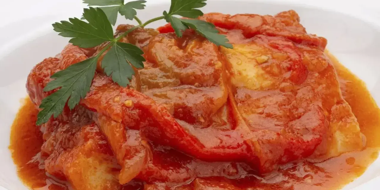 Bacalao a la riojana, un plato tradicional con trozos de pescado blanco cubiertos en una salsa roja de pimientos y tomate, adornado con perejil fresco.