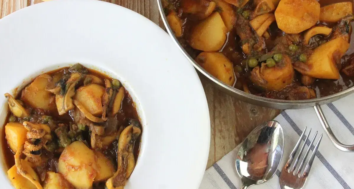 Un plato de papas con choco, un guiso casero con trozos de patata, guisantes y calamares en una rica salsa.