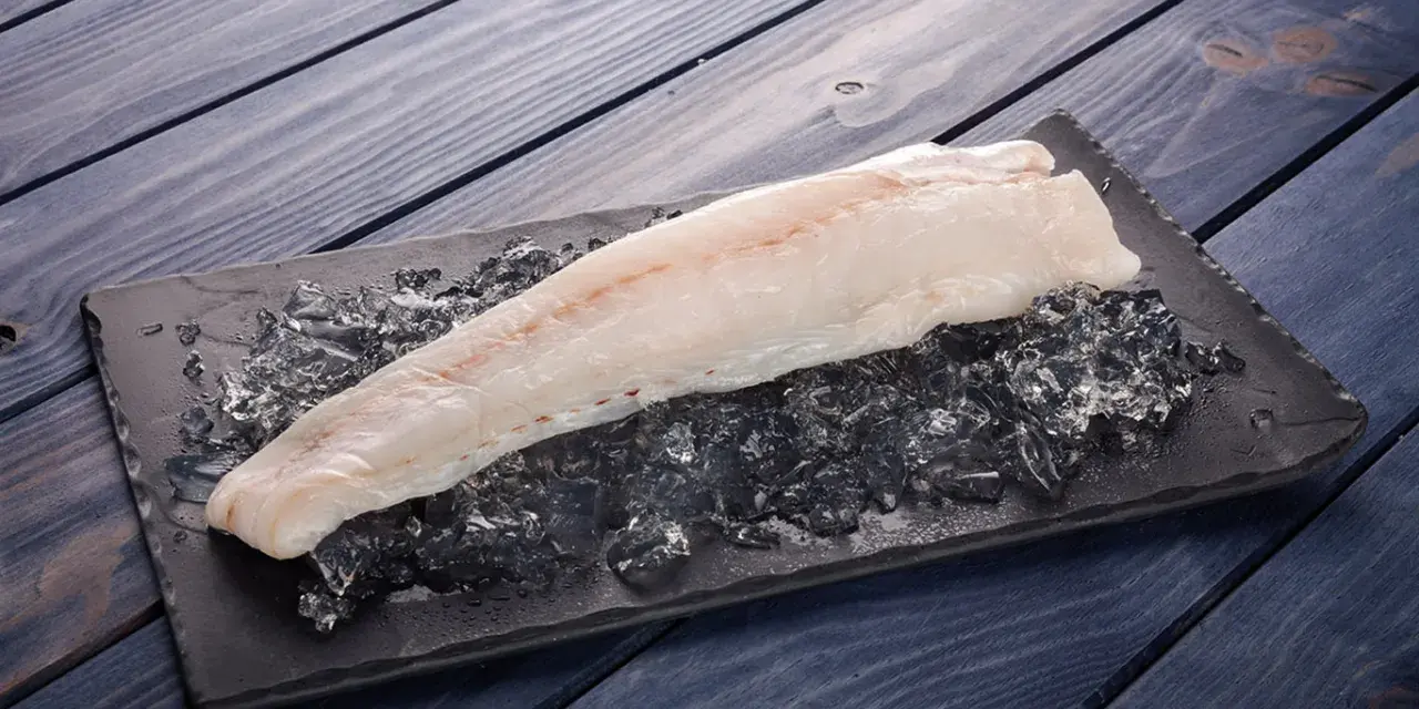 Filete de pescado rosado fresco sobre hielo picado en una tabla negra, listo para cocinar.