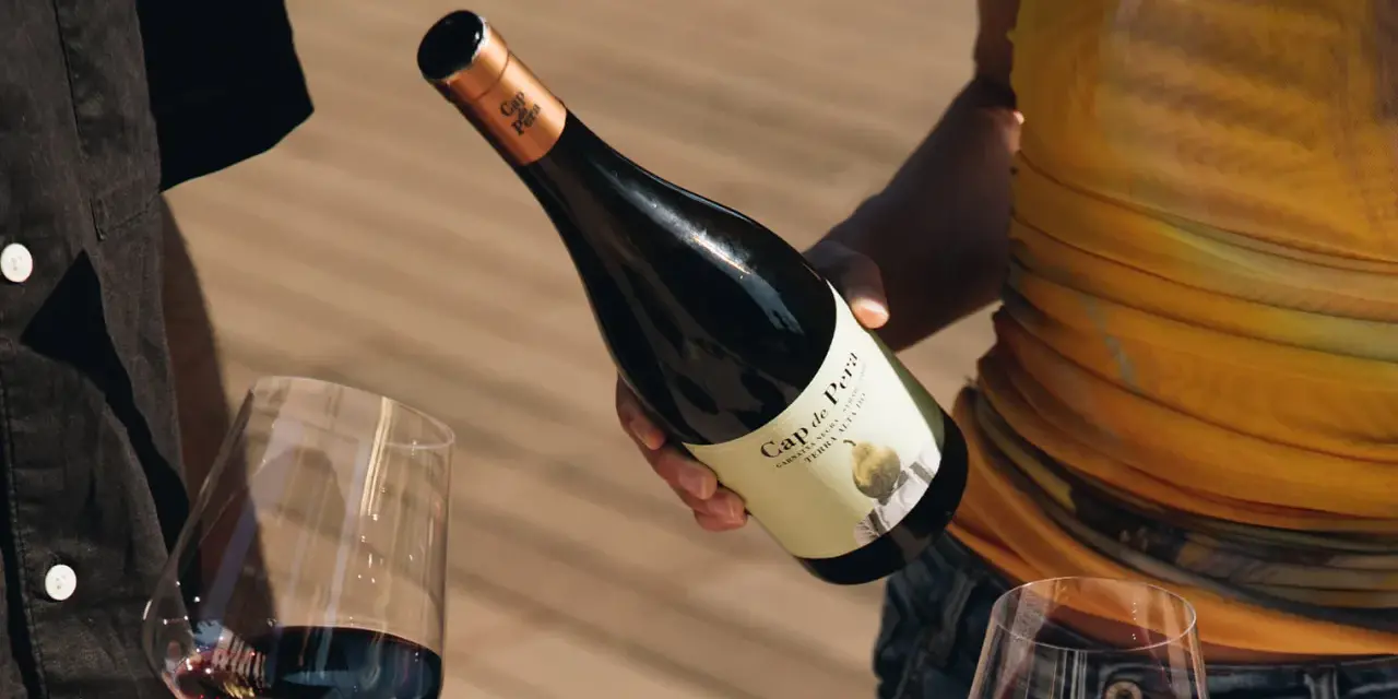 Manos sirven vino tinto de una botella Cap de Pera. Opiniones sobre "llàgrimes de tardor" y la experiencia.