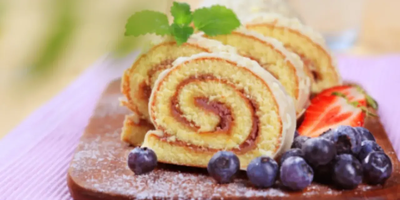Brazo de gitano en rodajas con fresas y arándanos sobre tabla de madera.
