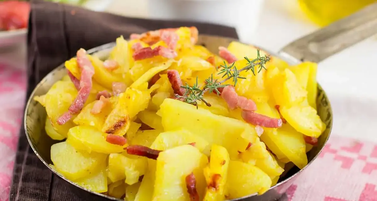 Patatas al microondas con trocitos de bacon crujiente y romero fresco, servidas en una sartén metálica. ¡Un plato sencillo y delicioso!
