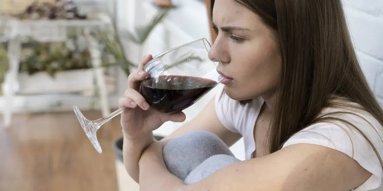 Mujer pensativa bebe vino tinto, recordando que el vino engorda.