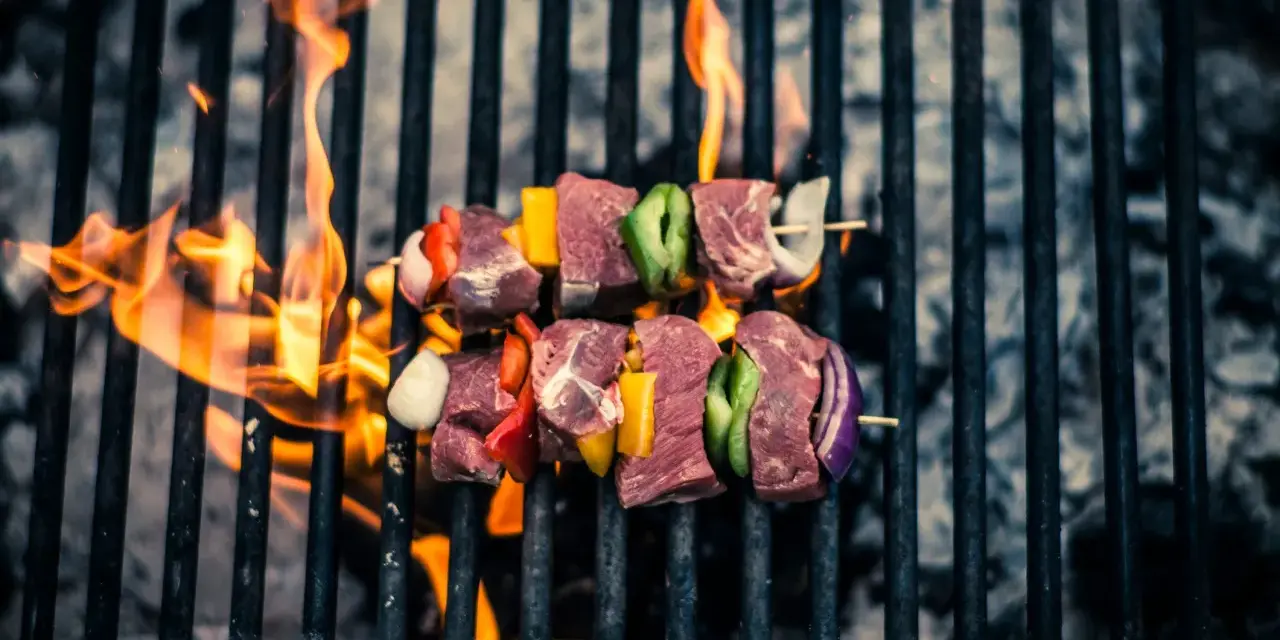 Brochetas de carne y verduras sobre una parrilla con llamas. Así es como se prepara una deliciosa barbacoa.