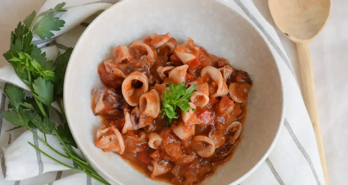 Deliciosos chipirones en salsa de tomate, servidos en un cuenco de cerámica, decorados con perejil fresco.